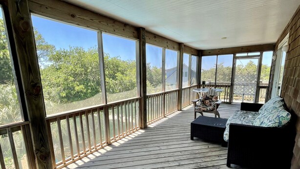 Een overdekte veranda met een houten vloer, een comfortabele bank en een tafel met stoelen.