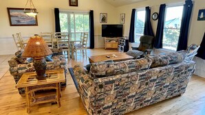 Een woonkamer met een gestreept bankje, een houten salontafel, een televisie en een eethoek met stoelen en een tafel.