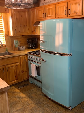 Una cocina con armarios de madera, un refrigerador azul, una estufa y un lavamanos.