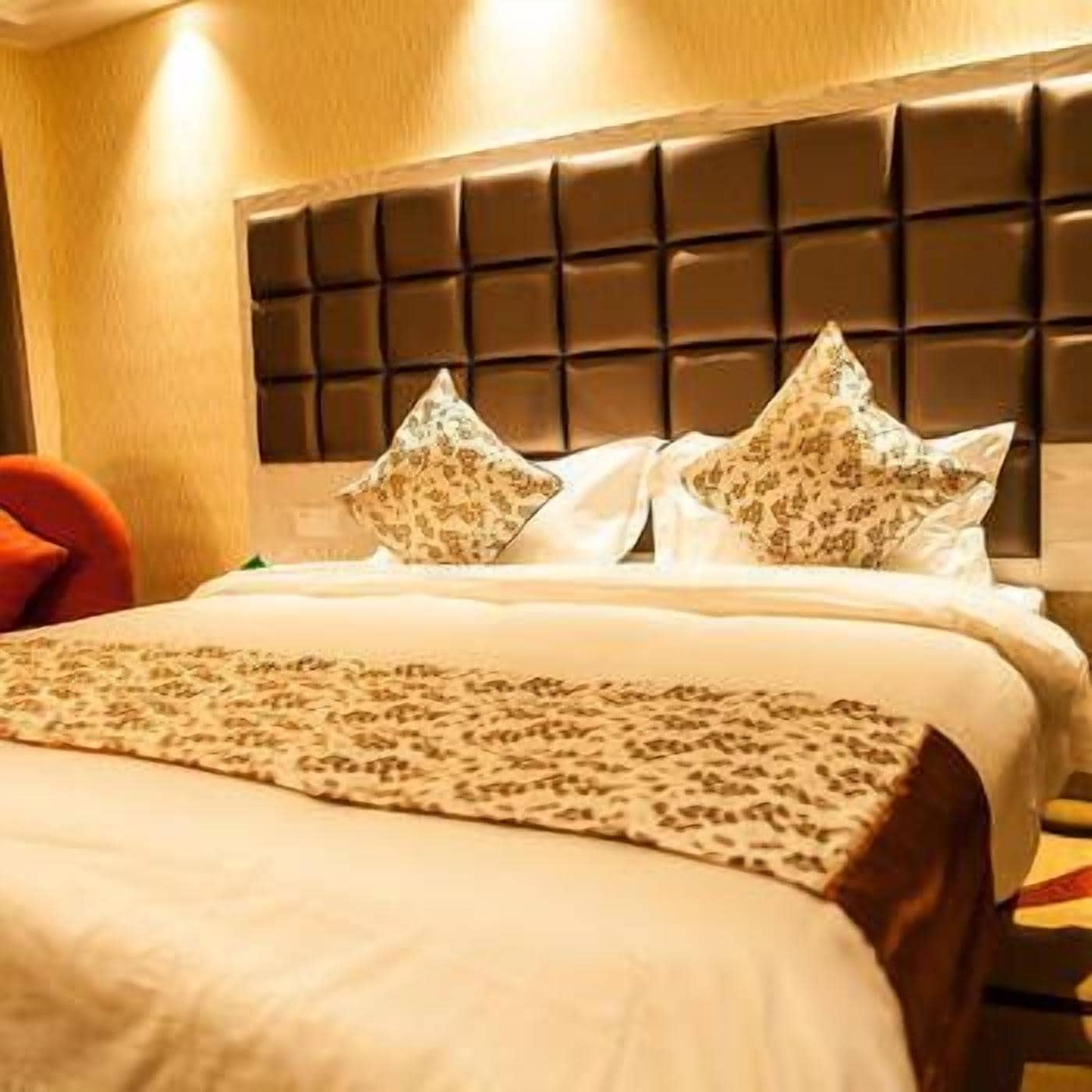 A hotel room with a tufted headboard, a bed with patterned bedding, and a red chair.