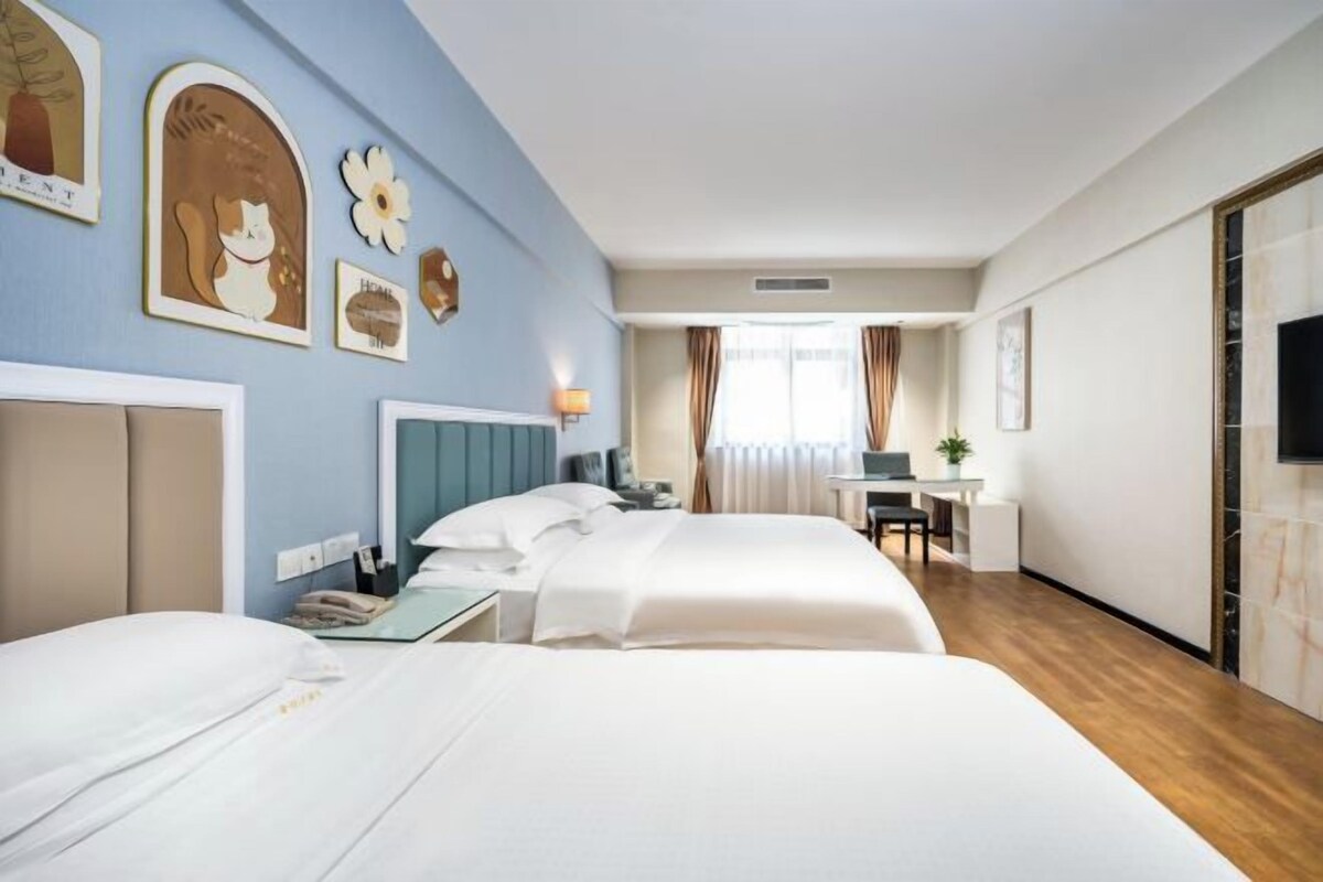 A hotel room with two beds, a desk, a chair, a TV, and artwork on the walls.