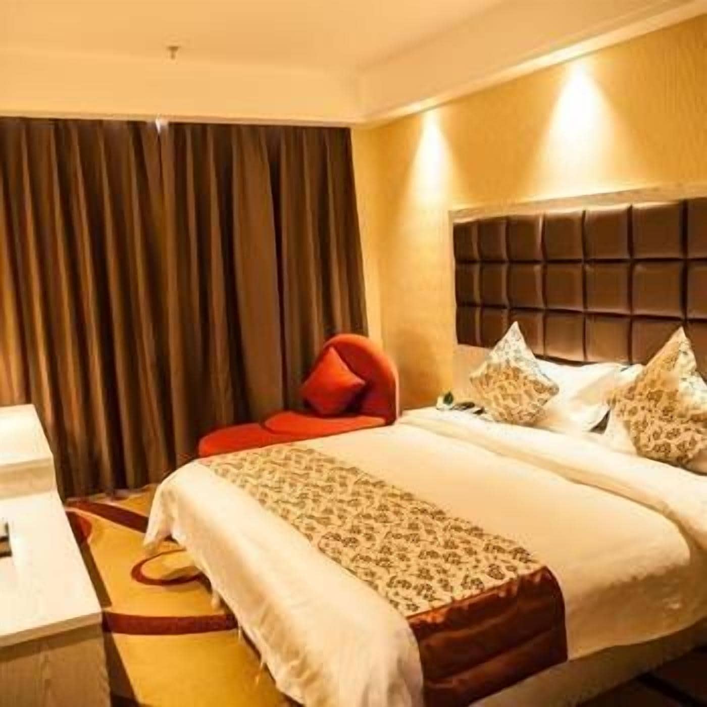 A hotel room with a bed, a red chair, a bedside table, and a curtain.