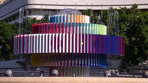 Un edificio moderno con una estructura cilíndrica distintiva y franjas verticales de varios colores.