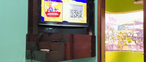 A television mounted on a wall with a QR code, a basket with snacks, and a white appliance below it.