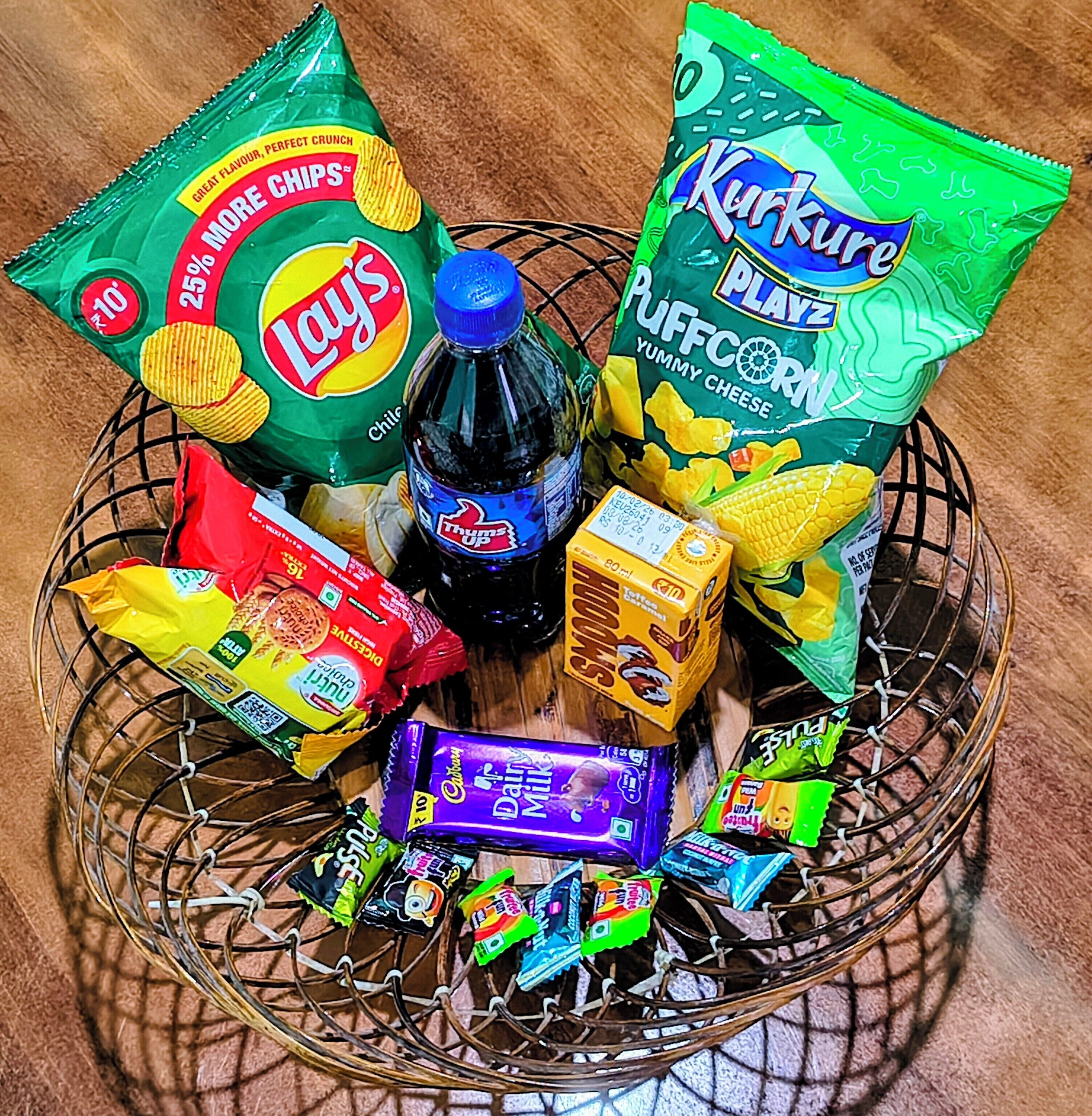 Un panier contenant des en-cas comme des chips Lay’s, du pop-corn Kurkure et du chocolat au lait Cadbury.
