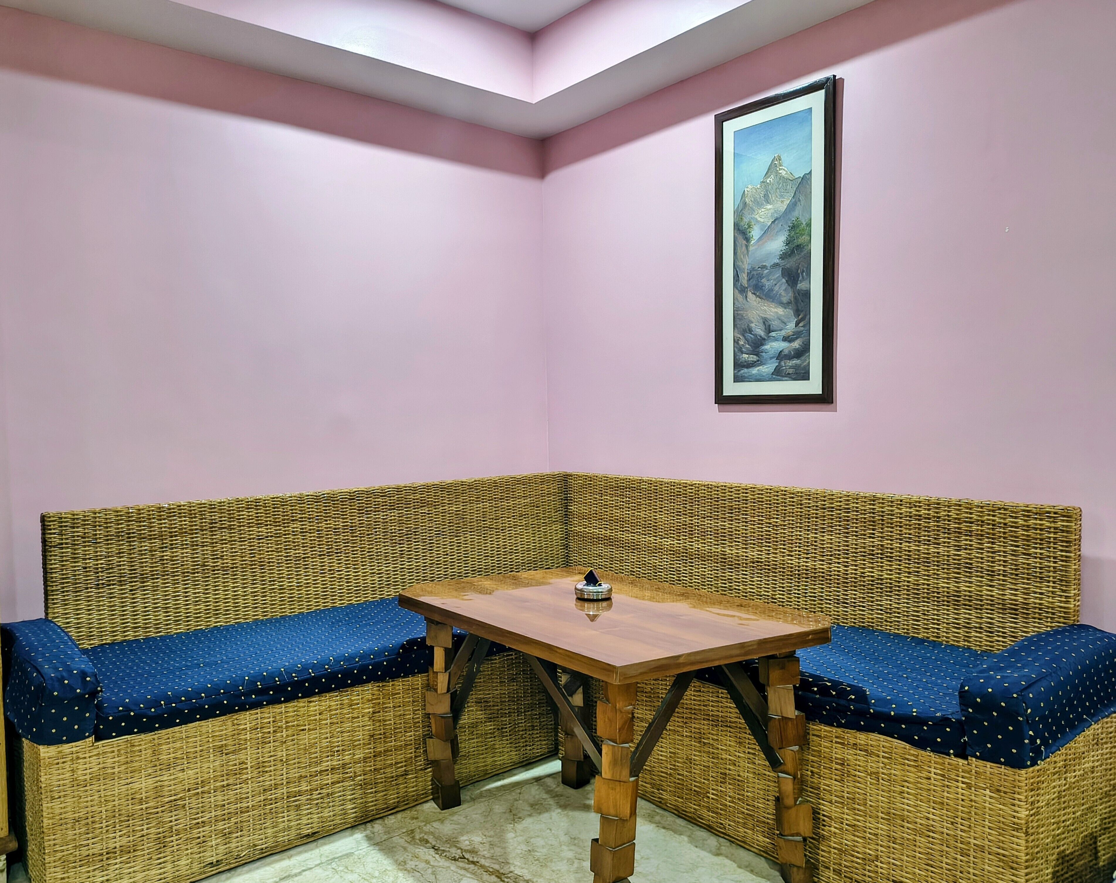 A corner room with a wicker sofa, a wooden table, and a framed painting on the wall.