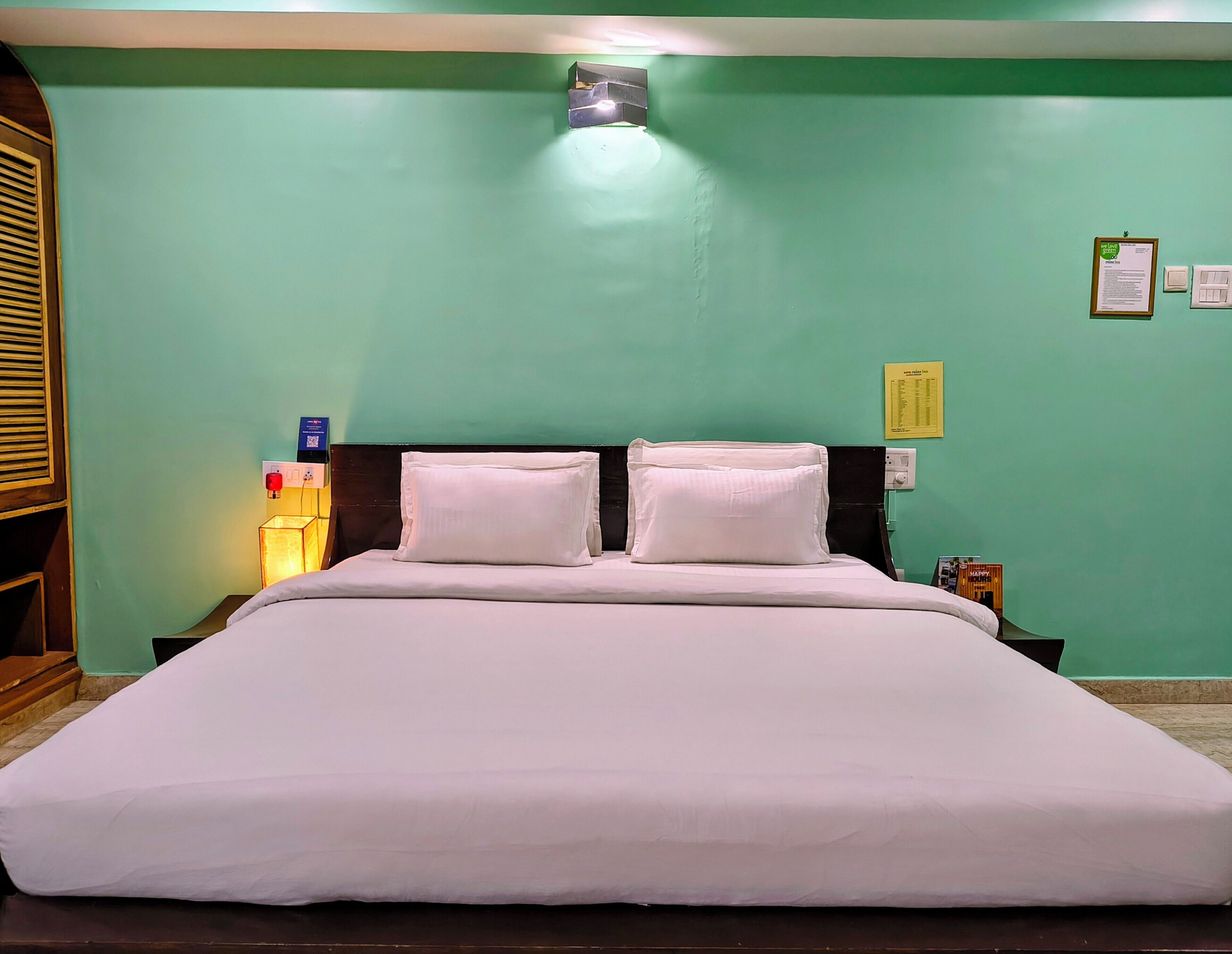A bed with white bedding, a nightstand with a lamp, and a wall-mounted light fixture.