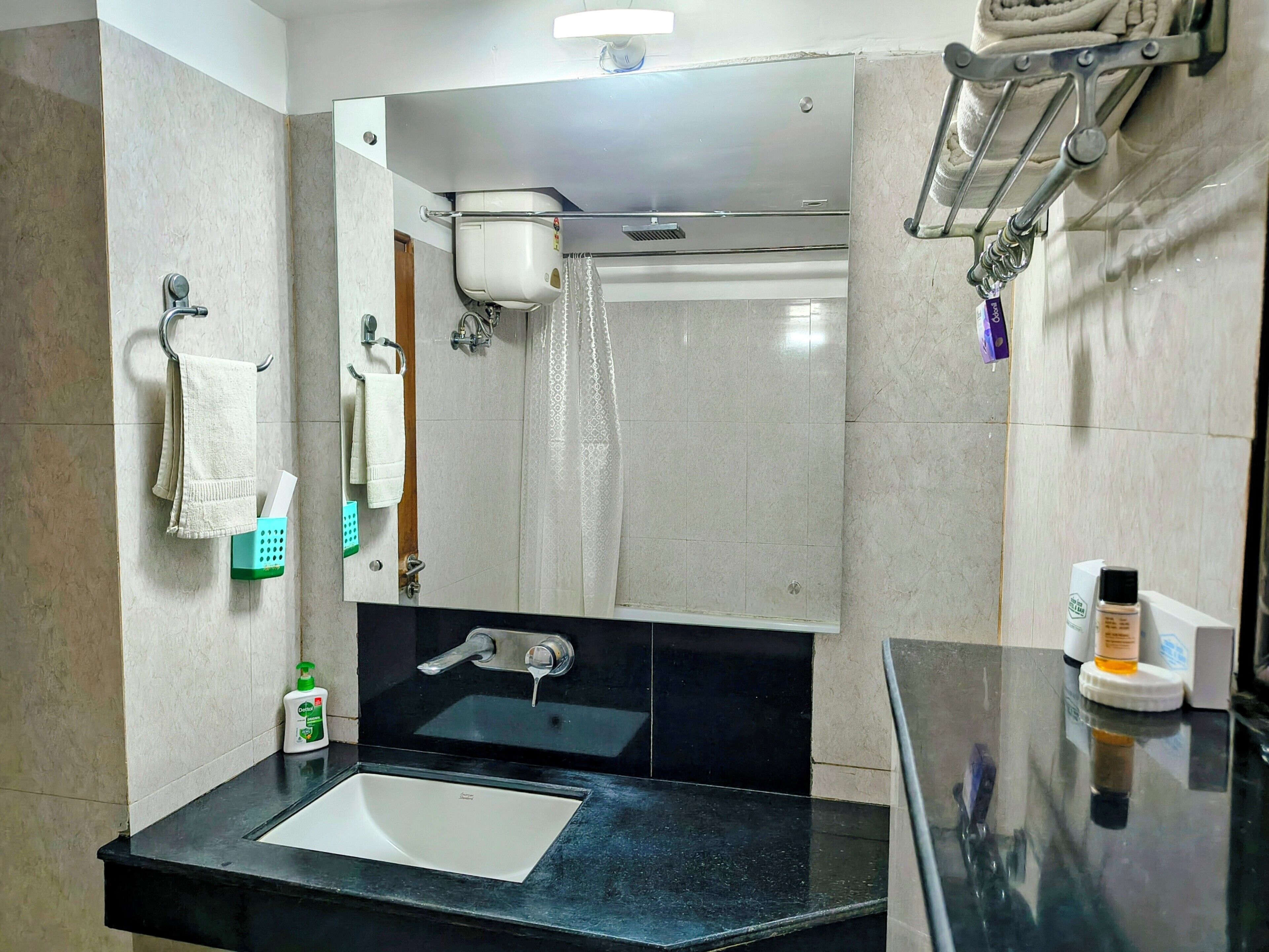 Un baño con lavamanos negro, espejo, toallero, ducha y dispensador de jabón.