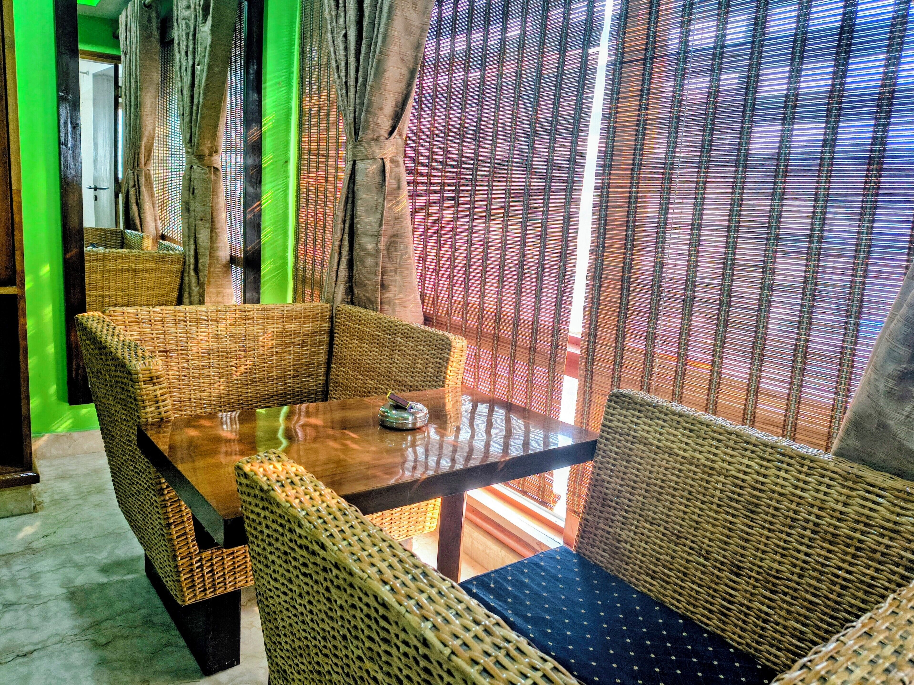 A room with wicker furniture, a wooden table, and a view through patterned curtains.