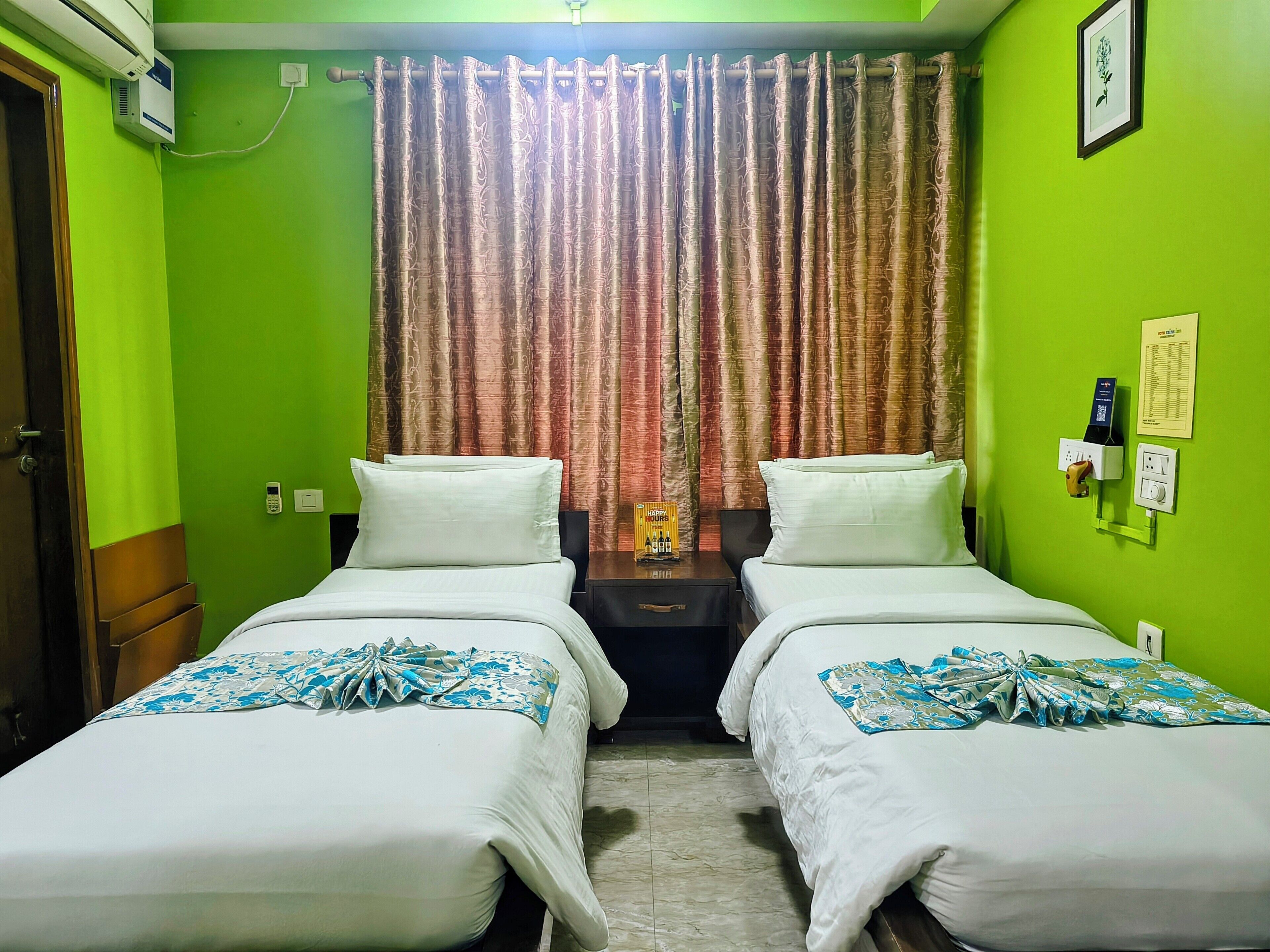 A room with two beds, a green wall, a curtain, a nightstand, and a wall-mounted phone.