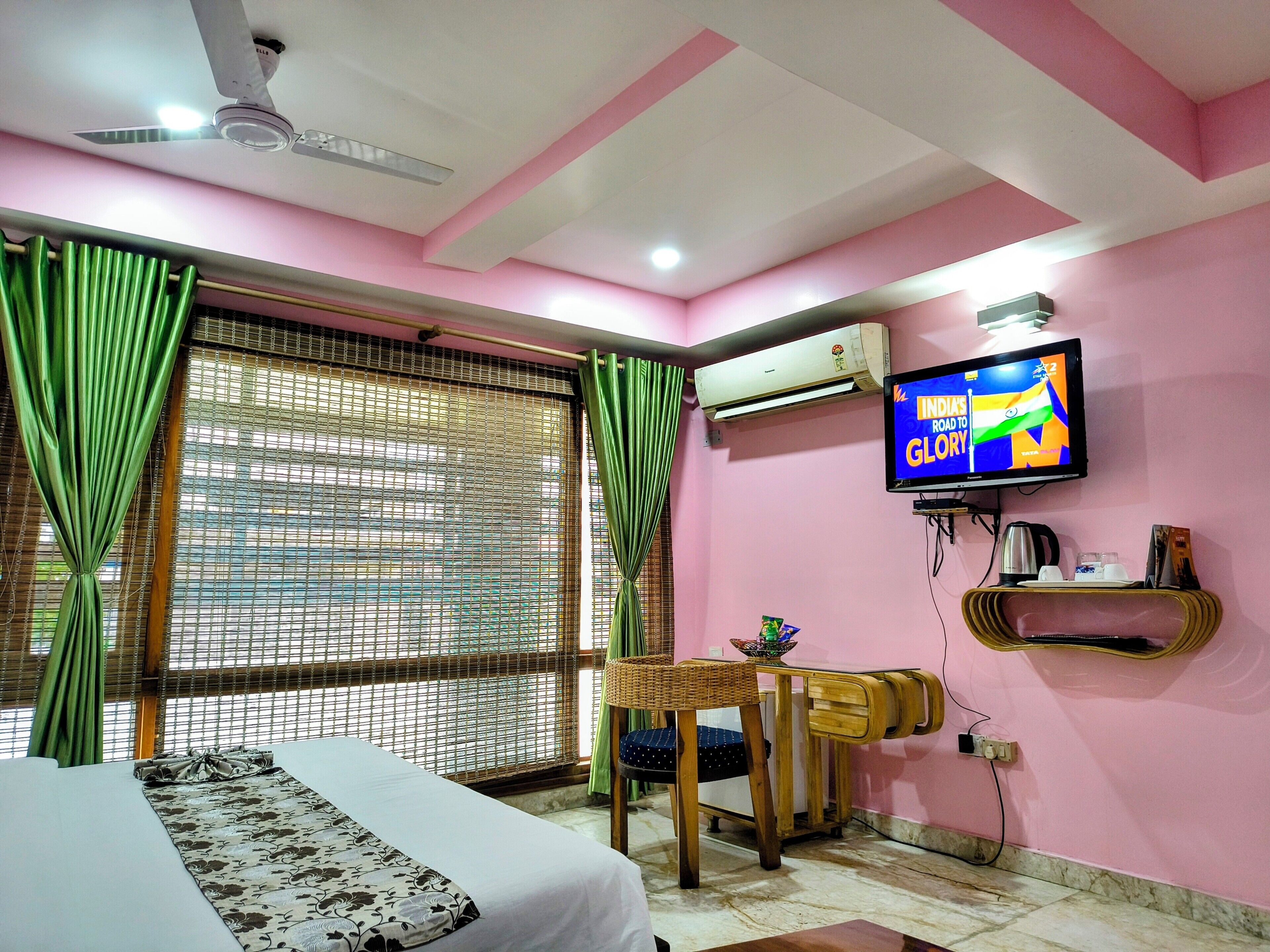 A room with a bed, a television displaying a program, an air conditioner, and a window with curtains.