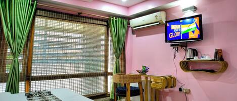 A room with a bed, a television displaying a program, an air conditioner, and a window with curtains.