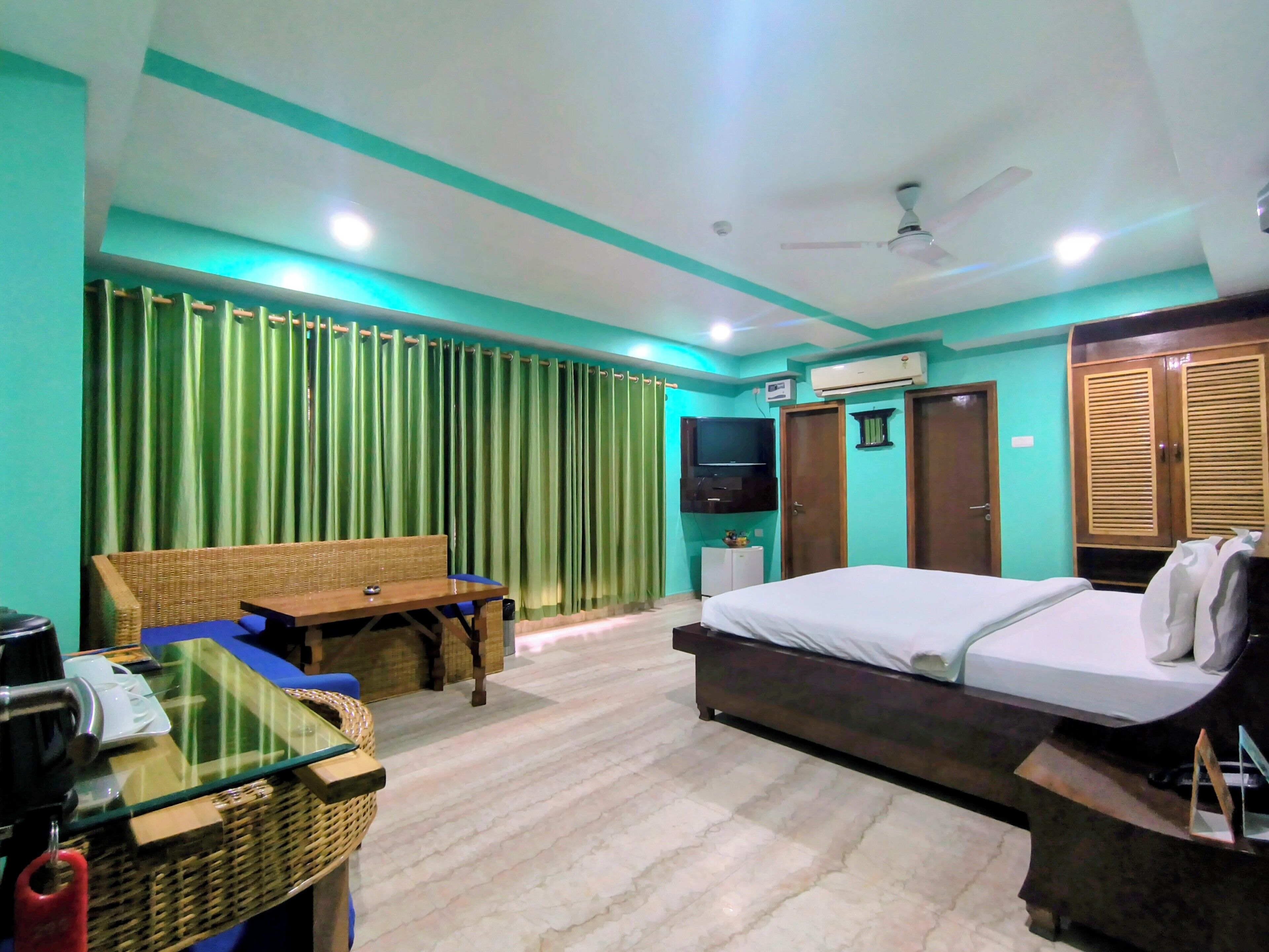 A hotel room with a bed, a sofa, a television, an air conditioning unit, and a ceiling fan.