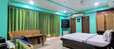 A hotel room with a bed, a sofa, a television, an air conditioning unit, and a ceiling fan.