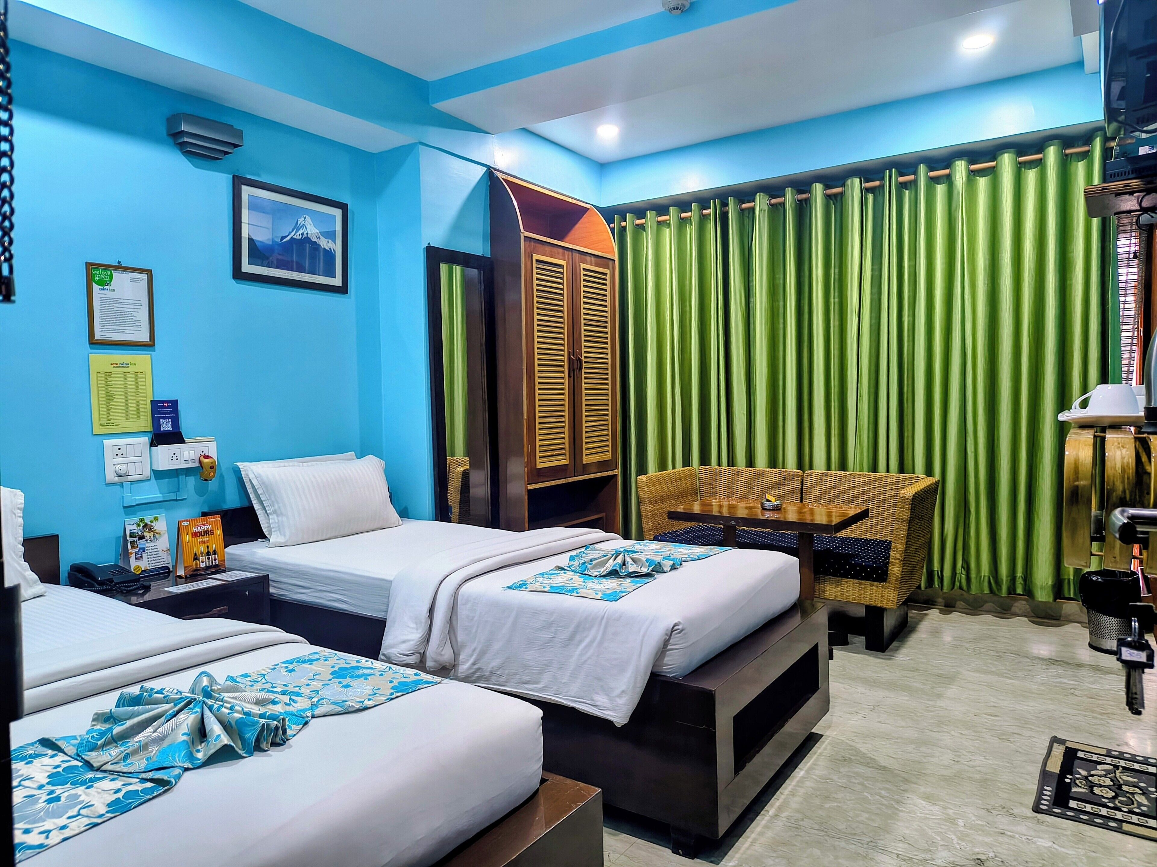 A hotel room with two beds, a green curtain, a wicker sofa, and a mounted television.