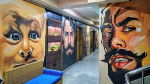 Un pasillo con grandes murales en las paredes, un sofá de mimbre con cojines azules y una barandilla de metal.