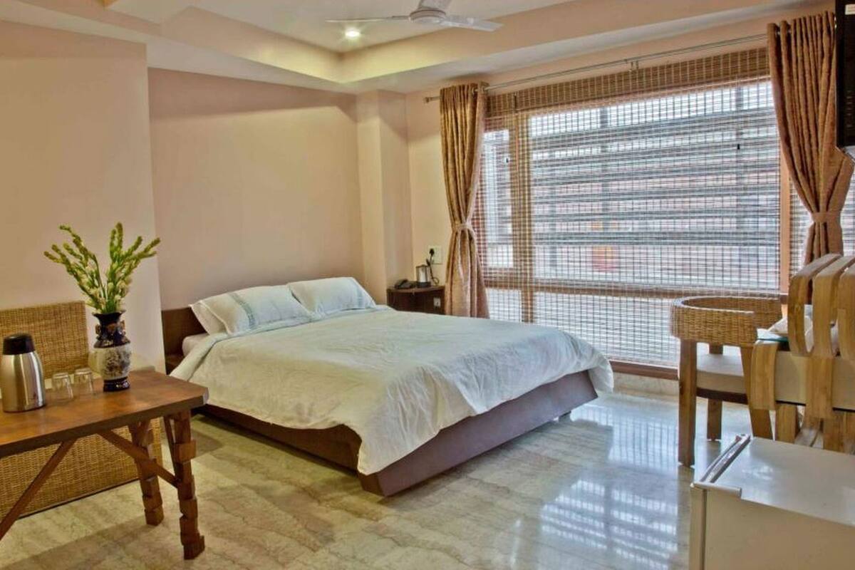 A bedroom with a bed, bedside table, lamp, and a view of the outside through a window with curtains.