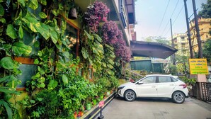 Un coche blanco aparcado frente a un edificio con una pared verde cubierta de plantas y un cartel que indica un hotel, bar y restaurante.