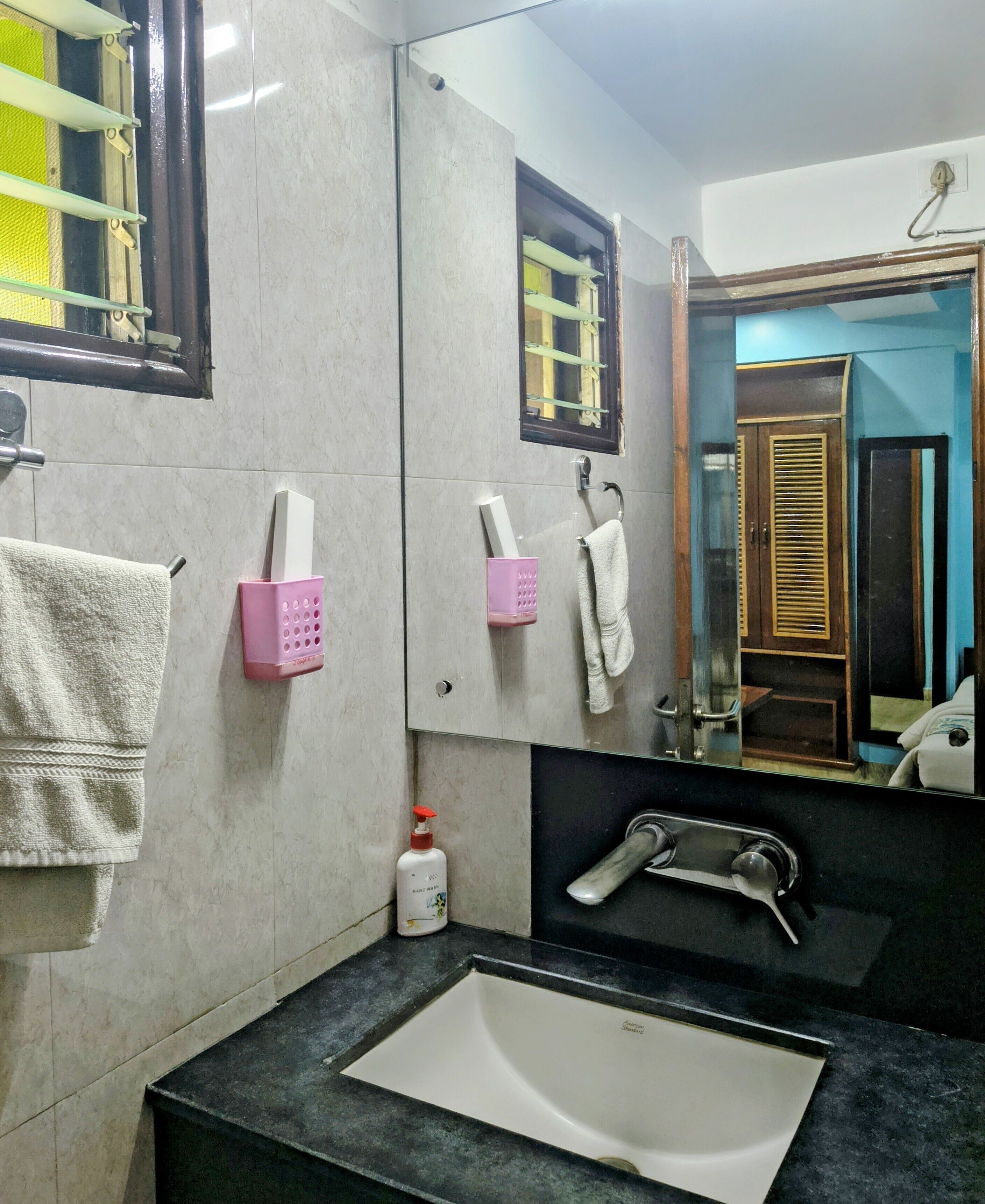 Un baño con lavamanos blanco, espejo, toallero y jabón de manos.