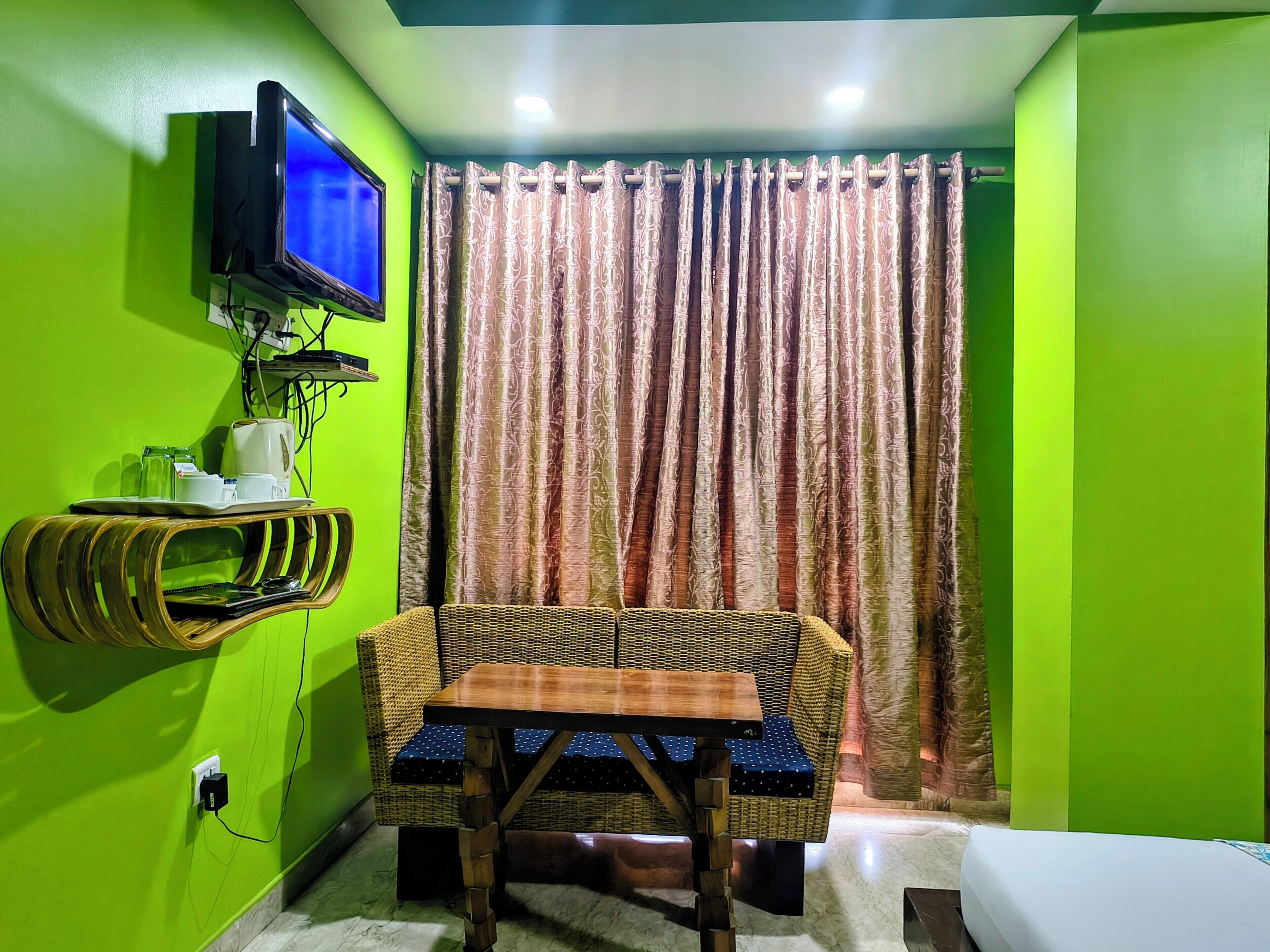A room with a television mounted on the wall, a wicker chair with a table, and a curtain.
