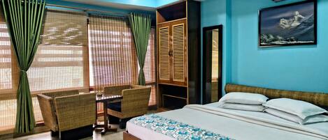 A bedroom with a bed, a desk, and chairs, a wardrobe, and a painting on the wall.