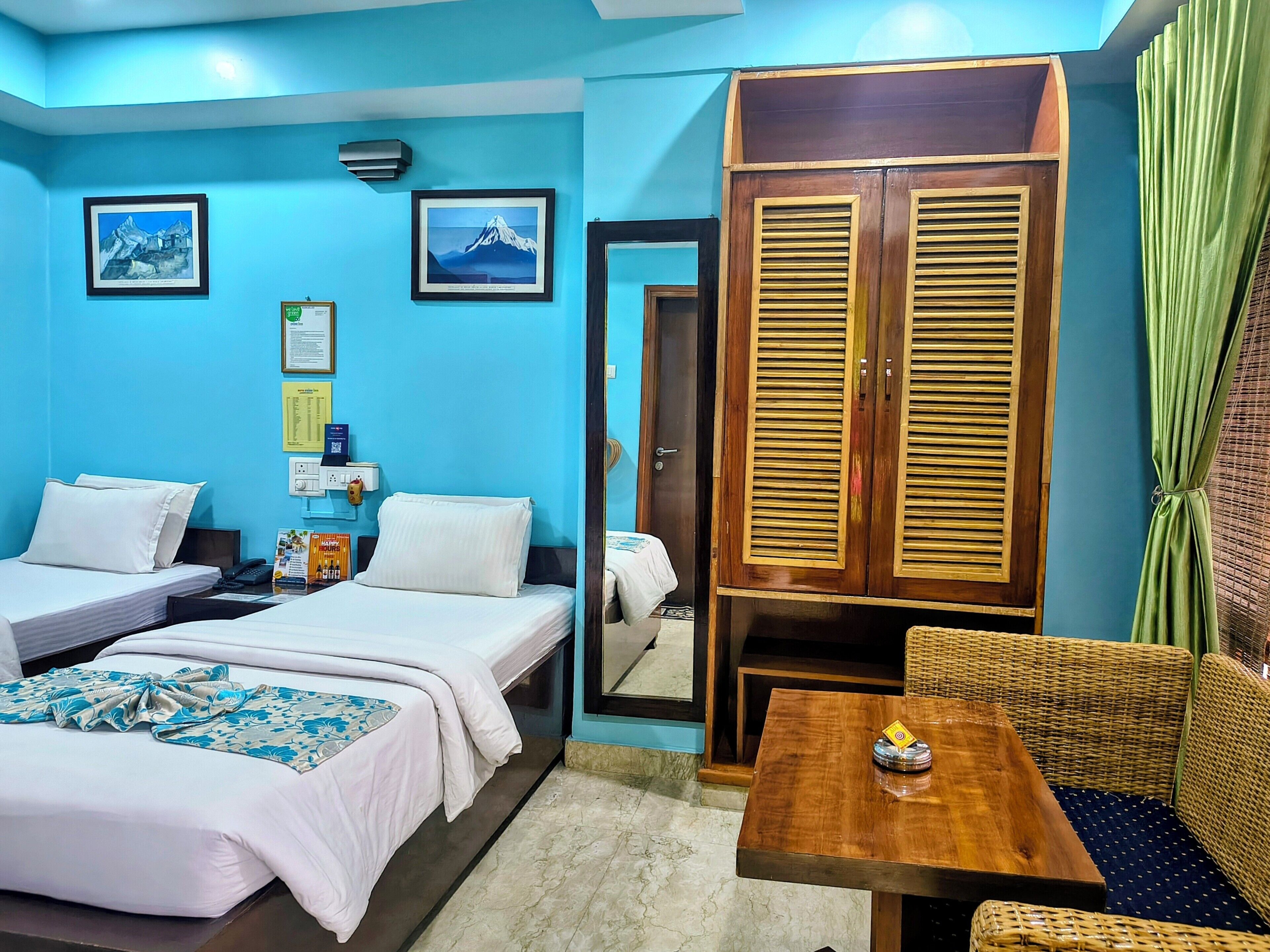 A hotel room with two beds, a wooden wardrobe, a small table, and a wicker sofa.