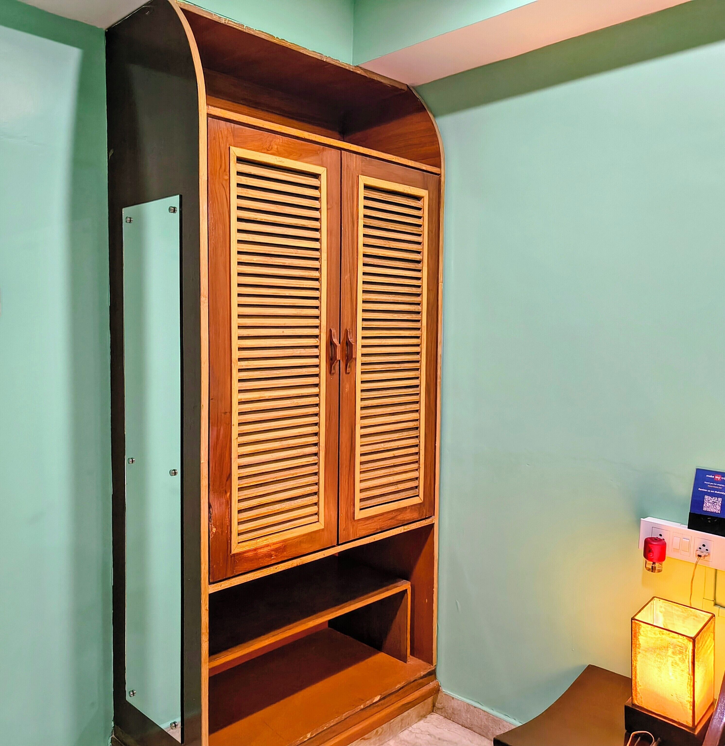 A wardrobe with two doors and a shelf, in a room with teal walls and a small table with a lamp.
