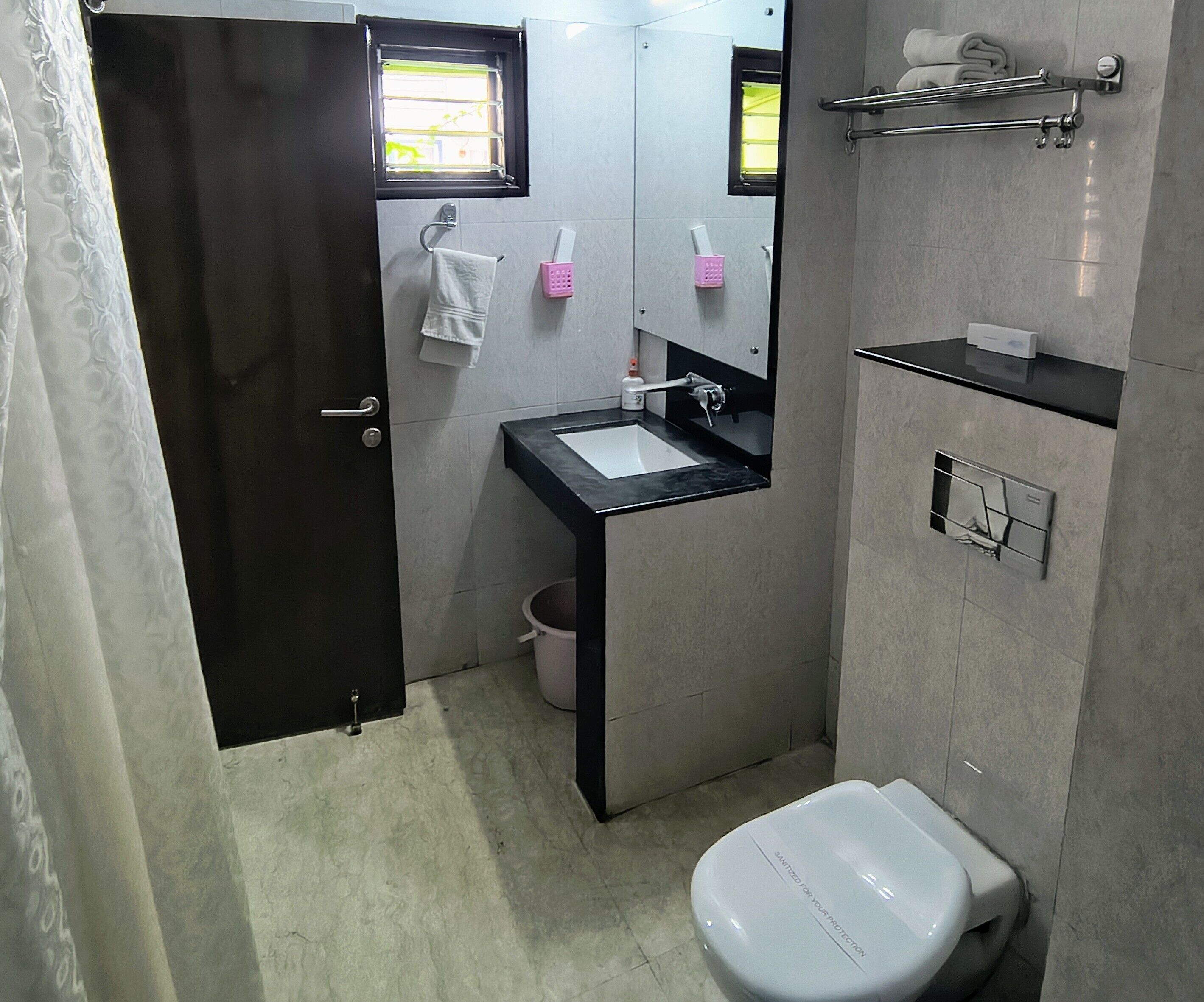A bathroom with a toilet, sink, and mirror. There is a towel rack above the sink and a window above the mirror.