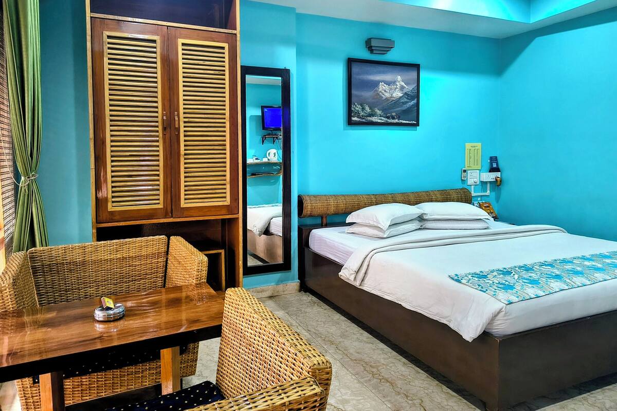 A room with a bed, a wooden wardrobe, a wicker table, and a mirror.