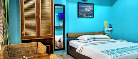 A room with a bed, a wooden wardrobe, a wicker table, and a mirror.
