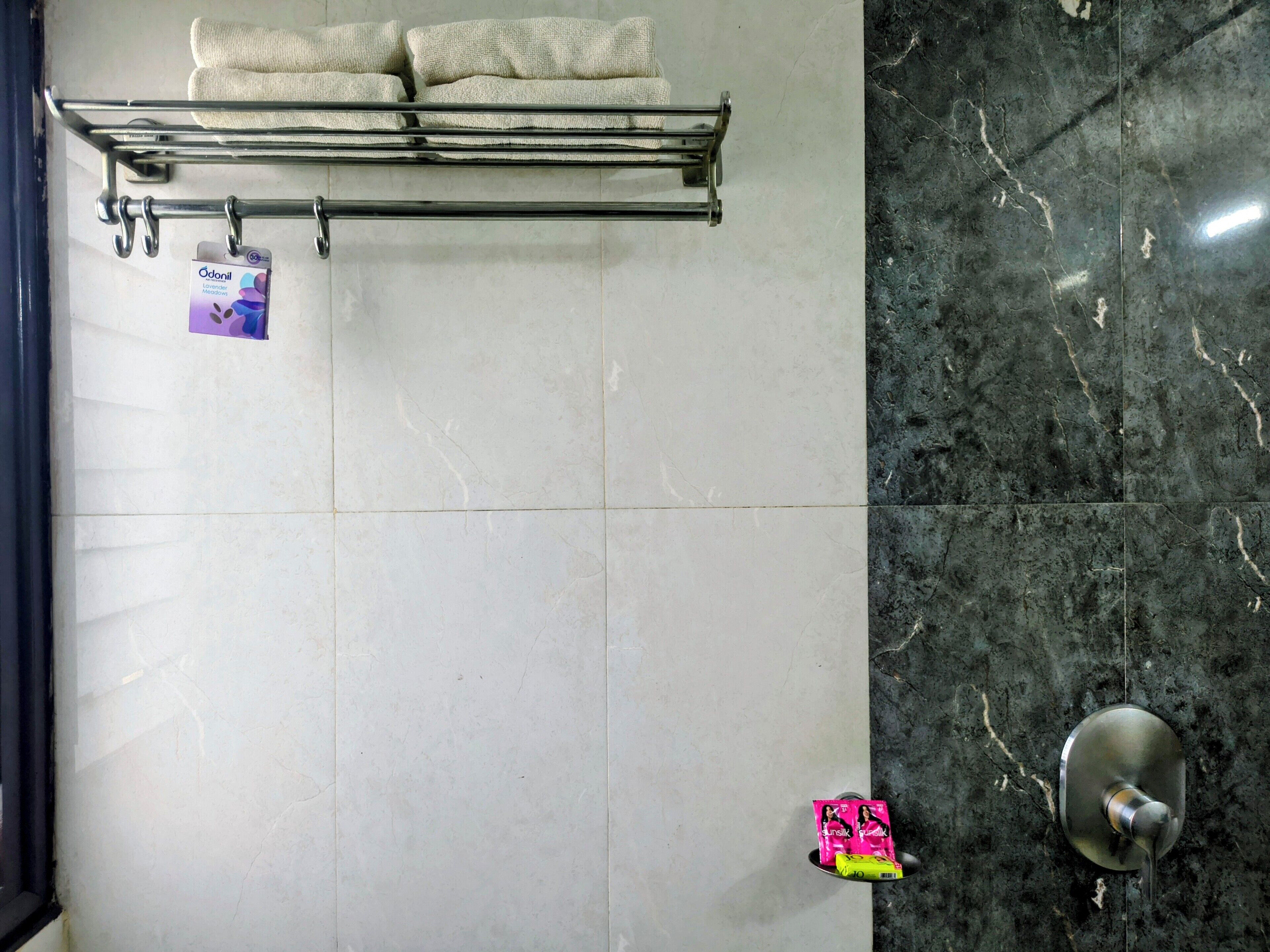 A bathroom with a towel rack, a soap dispenser, and a marble wall.