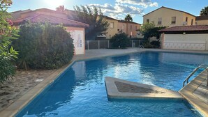 A swimming pool with a stone edge, surrounded by greenery and residential buildings. - Villa T3, private terrace & parking. Wifi Fibre, Swimming pool, Shops, Beach 50m! (Valras-Plage)