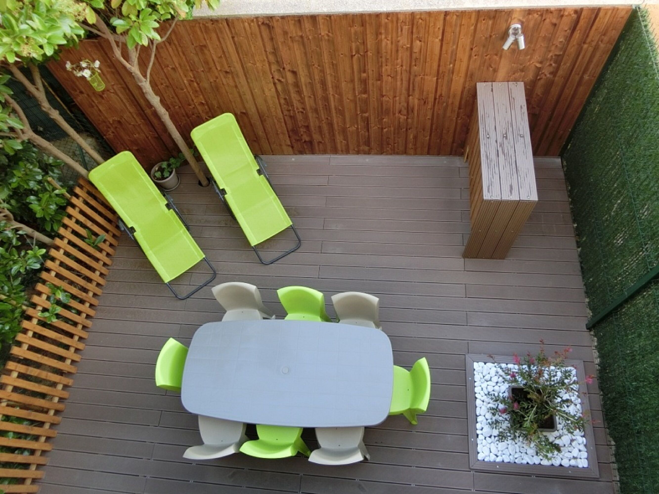 A wooden deck with a table and chairs, surrounded by a wooden fence and a green hedge.