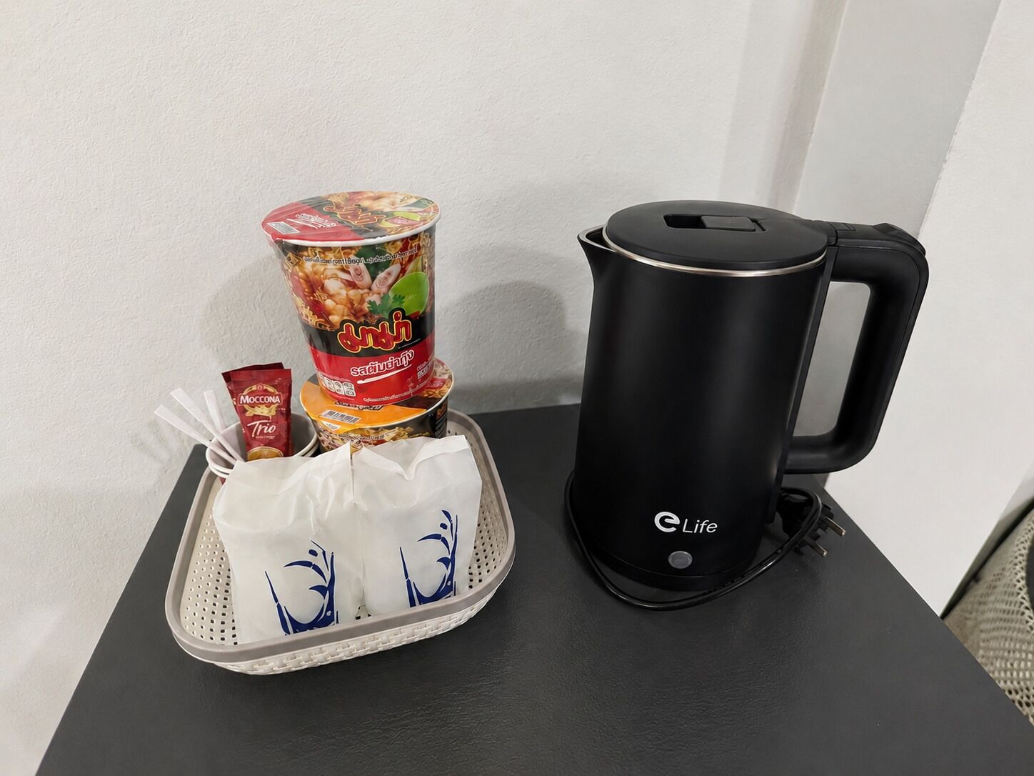 A black electric kettle with a Life logo, a tray with a white cloth and a red packet, and a can of food with a colorful label.