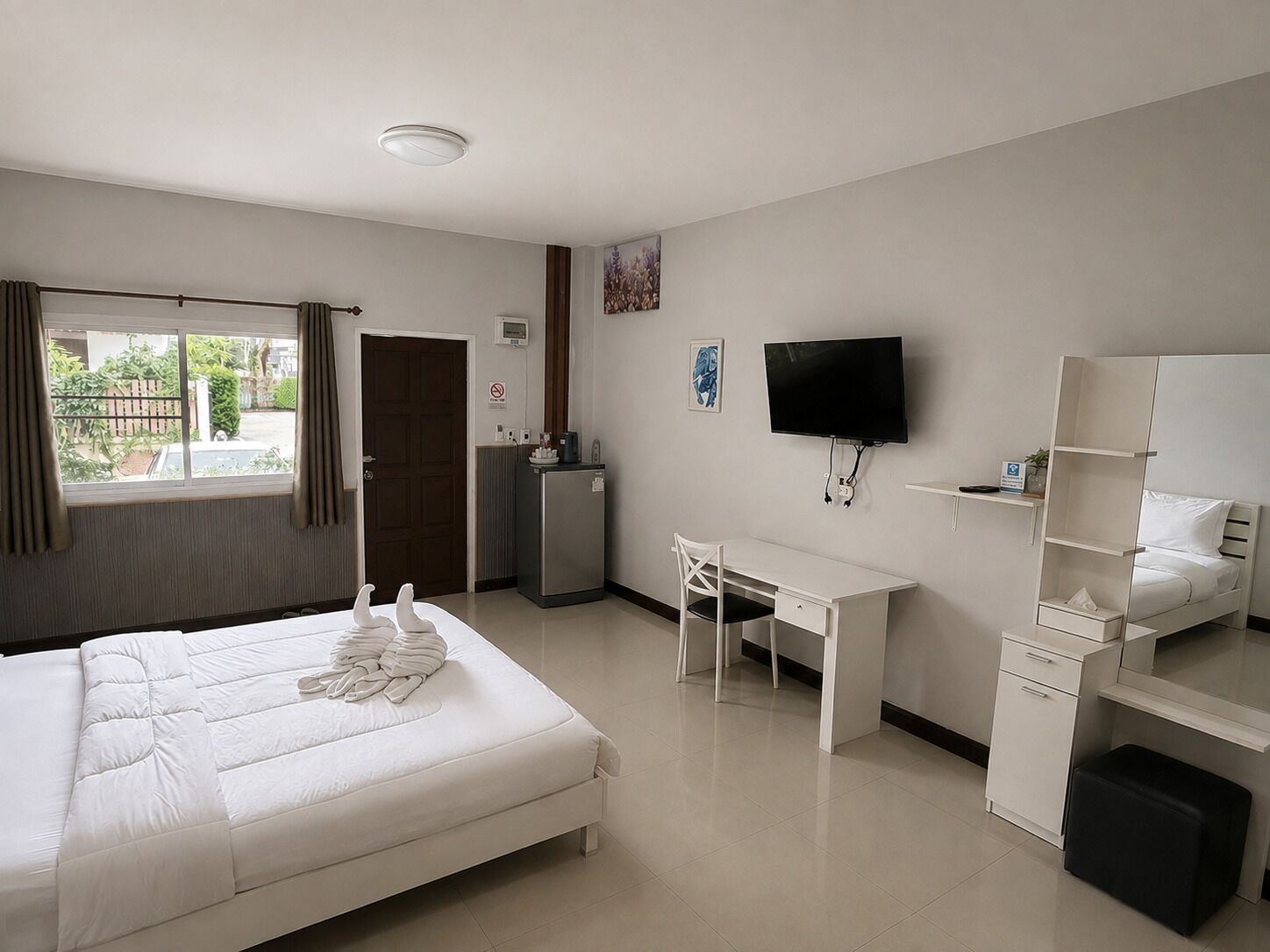 A hotel room with a bed, a desk, a television, a small kitchenette, and a window with curtains.