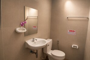 A bathroom with a sink, toilet, and a mirror. There are signs on the wall and a small shelf with a flower.