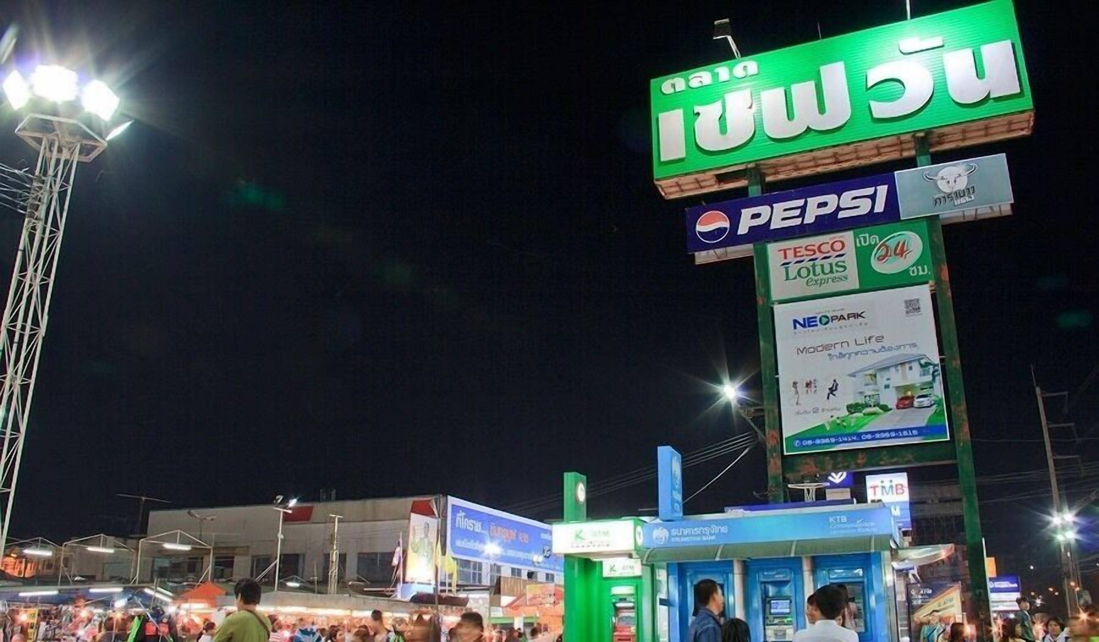 Une rue animée de nuit, avec une enseigne verte bien visible qui fait la publicité d’un magasin.