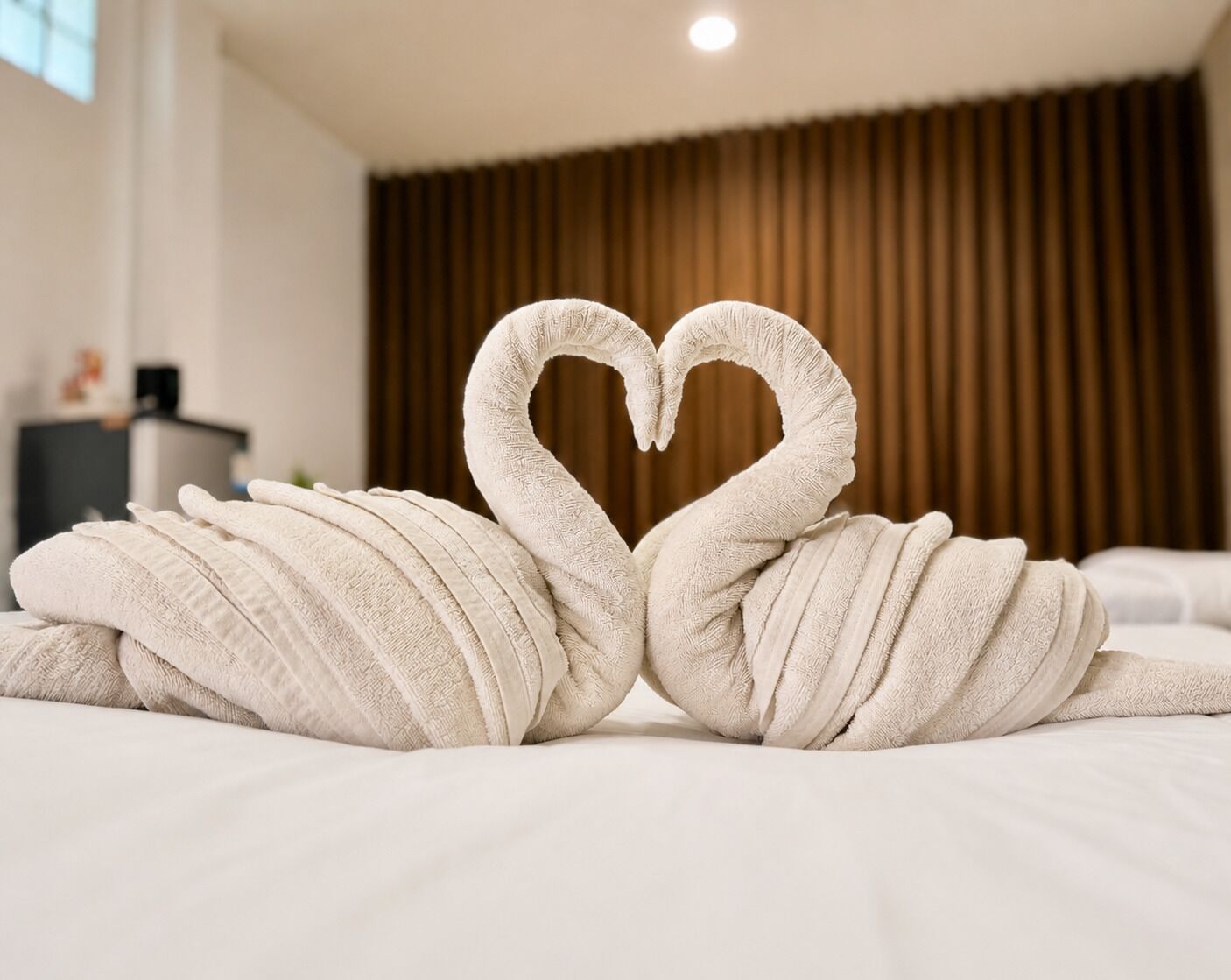 A bed with two towels arranged in the shape of a heart.
