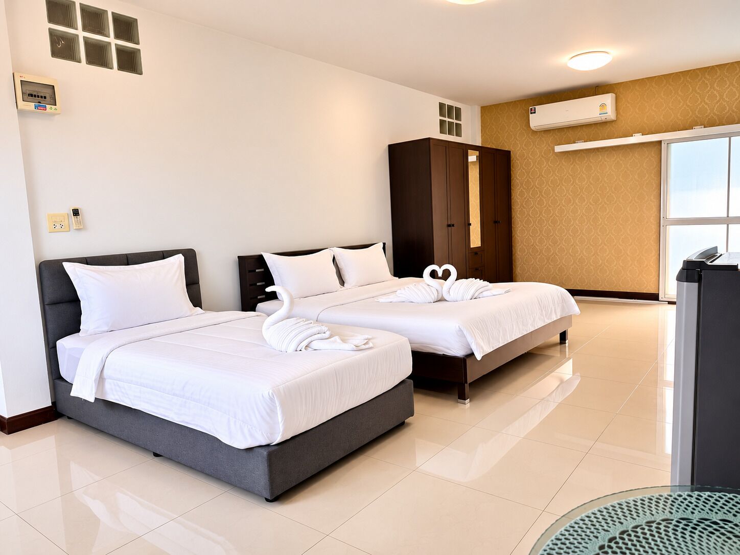 Habitación de hotel con dos camas, un armario, aire acondicionado y un escritorio con un cesto de basura.