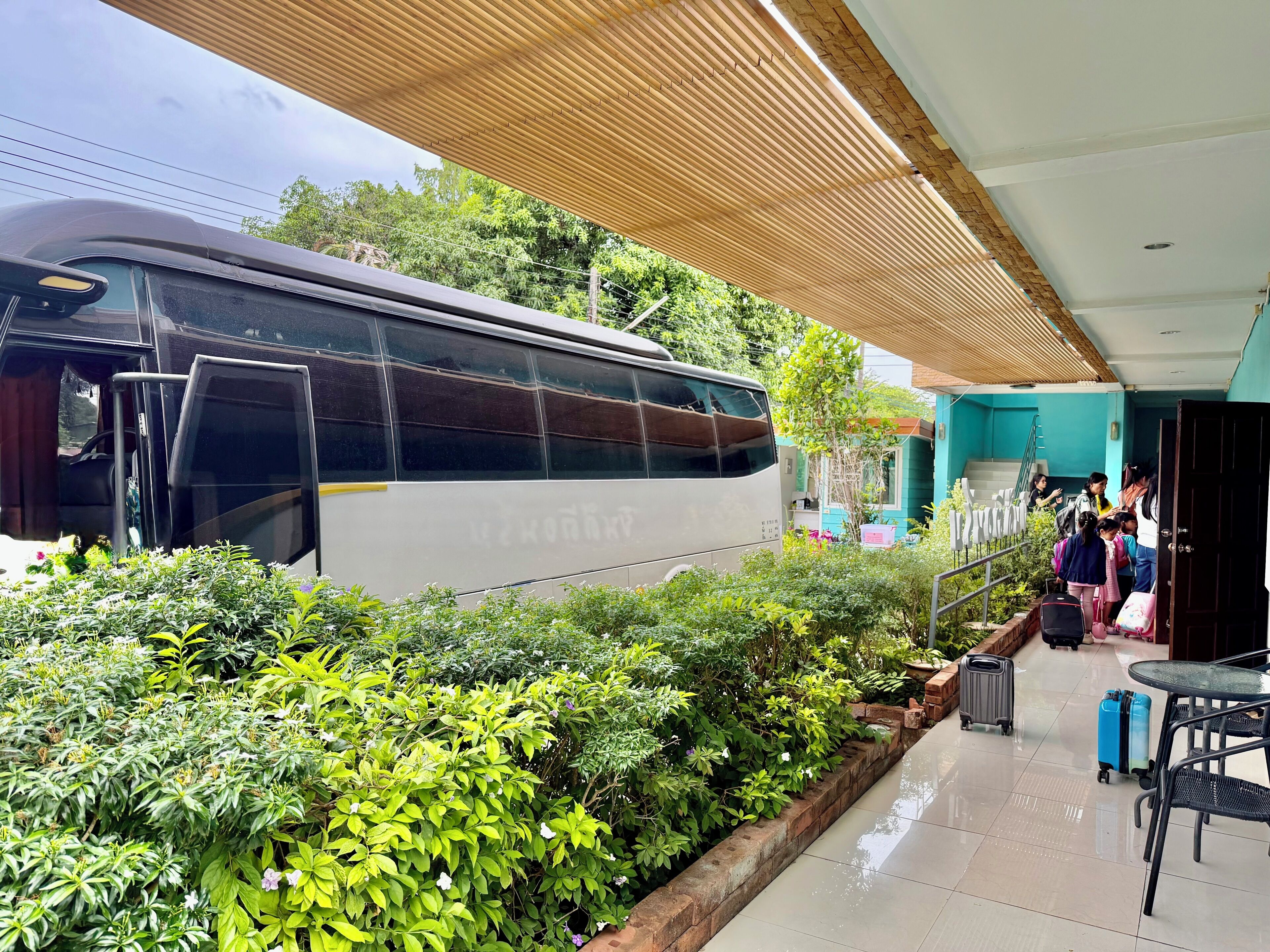 A bus parked in a covered area with greenery and a building in the background.