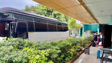A bus parked in a covered area with greenery and a building in the background.