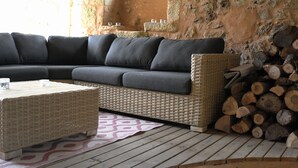 A modern living room with a sectional sofa, a woven coffee table, and a stack of firewood. - Rent Gite Casalissa house with heated pool in Perigord Noir, Sarlat (Castels)