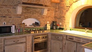 A kitchen with a stone wall, a microwave, a stove, and a sink. - Rent Gite Casalissa house with heated pool in Perigord Noir, Sarlat (Castels)