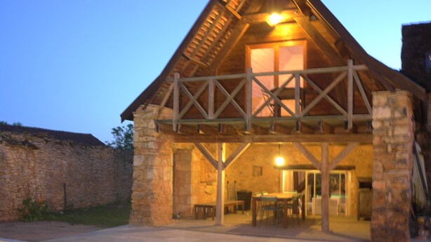 A stone building with a wooden balcony and a dining area inside. - Rent Gite Casalissa house with heated pool in Perigord Noir, Sarlat (Castels)