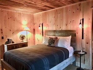 A wooden-paneled room with a bed, bedside lamps, a fan, and a small table. - Artisan-crafted Magic on Lake Superior (Lutsen)
