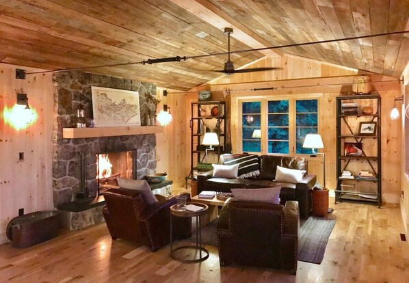 A cozy cabin interior with a stone fireplace, wooden walls, a leather sofa, and a large window. - Artisan-crafted Magic on Lake Superior (Lutsen)