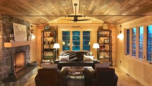 A cozy cabin interior with a stone fireplace, wooden walls, a leather sofa, and a bookshelf. - Artisan-crafted Magic on Lake Superior (Lutsen)