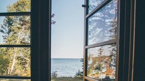 A window with a view of a lake, two red Adirondack chairs, and a child playing. - Artisan-crafted Magic on Lake Superior (Lutsen)