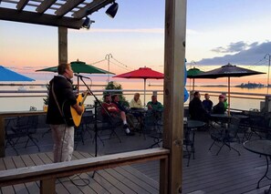 A musician performing on a wooden deck with tables and chairs, overlooking a body of water. - Artisan-crafted Magic on Lake Superior (Lutsen)