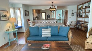 Un salon chaleureux avec un canapé bleu, une table basse en bois et, au fond, un coin repas.